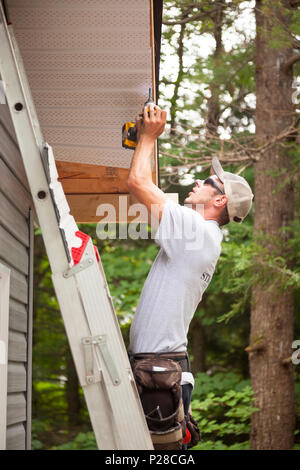 Un lavoratore con un trapano per installare intradossi. Foto Stock