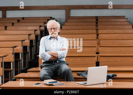 Capelli grigi professore in seduta vuota sala conferenze con bracci incrociati Foto Stock