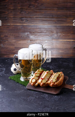 Foto di due bicchieri di birra, hot dogs, pallone da calcio Foto Stock