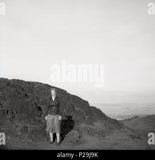 1951, lady walker in piedi da un picco roccioso sulle colline sopra Edimburgo, Scozia. Foto Stock
