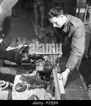 Degli anni Cinquanta, storico, un falegname o un falegname in un workshop in fabbrica utilizzando macchinari meccanici in legno da taglio, Inghilterra, Regno Unito. Foto Stock