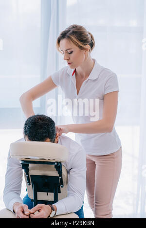 Attraente massaggiatrice facendo spalle massaggio sul sedile in ufficio Foto Stock