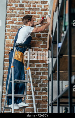 Giovani elettricista in piedi sulla scaletta e lavorando con spina Foto Stock