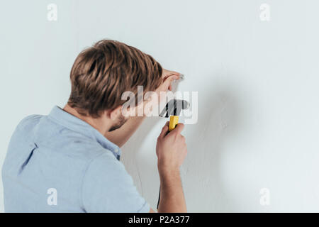 Vista posteriore del giovane uomo martellamento chiodo nella parete di casa Foto Stock