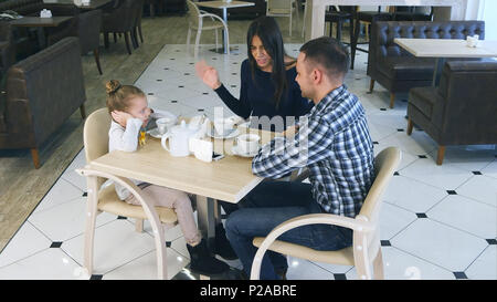 Indignato madre incolpando sulla figlia e suo marito in cafe. Littke ragazza di chiudere le sue orecchie. Foto Stock