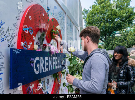 Coppia giovane immissione fiori alla base di di Grenfell Tower, per contrassegnare il un anno di anniversario del fuoco, Londra, Inghilterra, Regno Unito, 14 giugno 2018 Foto Stock