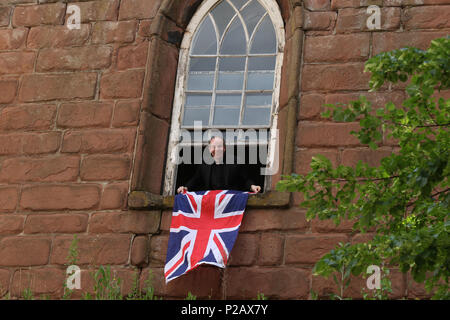 Un membro del clero si blocca su una bandiera dell'Union Jack prima di Sua Maestà la Regina Elisabetta II e Meghan Markle, duchessa di Sussex, visitare Chester sul loro primo impegno pubblico insieme. Chester, Cheshire, il 14 giugno 2018. Credito: Paolo Marriott/Alamy Live News Foto Stock