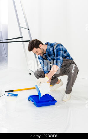 Uomo sorridente versando la vernice dalla benna in vernice plastica vassoio Foto Stock