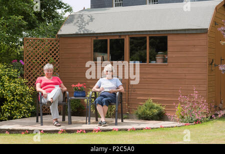 Due donne seduti su un patio giardino al di fuori di un fienile in legno in stile capannone. Foto Stock