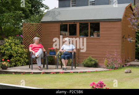 Due donne seduti su un patio giardino al di fuori di un fienile in legno in stile capannone. Foto Stock