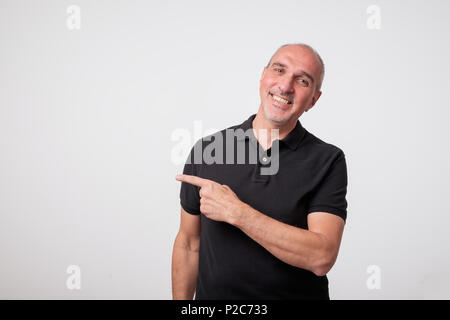 Bello maturare man in black t-shirt è rivolto lontano, guardando la fotocamera e sorridente Foto Stock