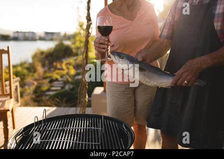 Coppia senior tenendo il pesce e un bicchiere di vino nel cortile posteriore Foto Stock