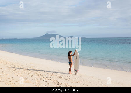 Donna in piedi con la tavola da surf in spiaggia Foto Stock