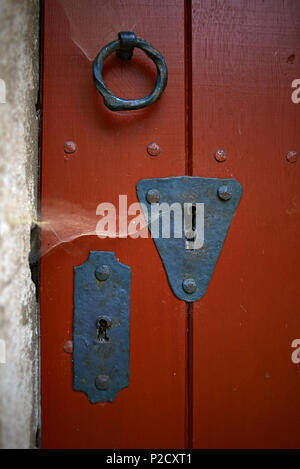 Close up di un di legno porta rossa con big black metal fori chiave in un arco. Ingresso a una piccola cappella nel Sauerland, Germania Foto Stock