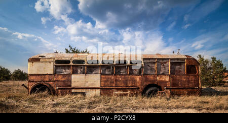 Abbandonato e rusty bus in un campo in una giornata soleggiata con cielo blu e nuvole nella centrale nucleare di Cernobyl la zona di alienazione Foto Stock