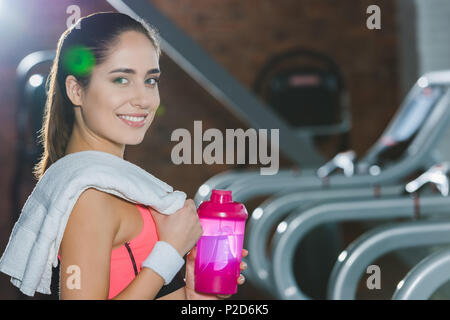 Sportivo da donna con shaker e asciugamano in mani contro il tapis roulant Foto Stock
