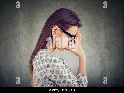 Vista laterale del casual ragazza in bicchieri tenendo la mano sulla fronte in pensieri profondi cercando miserabile con gli occhi chiusi. Foto Stock