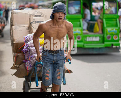 Un giovane uomo filippino tira un carico di merci entro il mercato del carbonio,Cebu City, Filippine Foto Stock