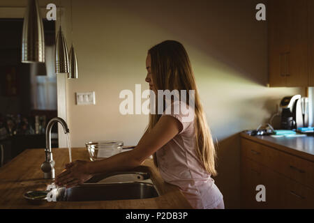 Ragazza in piedi in cucina lavando le mani sotto l'acqua del rubinetto Foto Stock