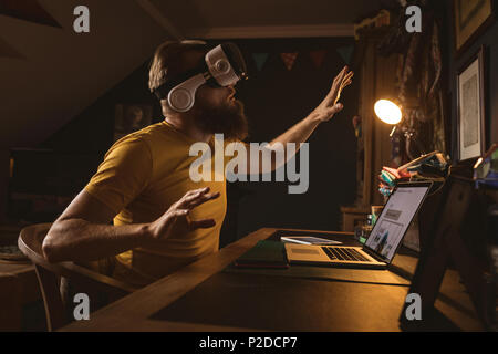 Uomo che indossa la realtà virtuale auricolare seduta anteriore del computer portatile Foto Stock
