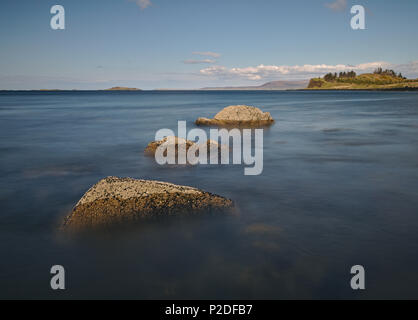 Tre scogli nell'oceano che conduce attraverso l'acqua verso una lontana isola all'orizzonte (lunga esposizione) Foto Stock