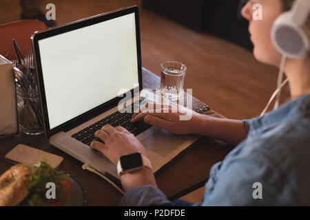 Donna ascoltare musica mentre si utilizza il portatile in tabella Foto Stock