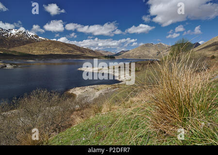 Loch Cluanie, Highlands scozzesi sotto un cielo blu con cime innevate sullo sfondo Foto Stock