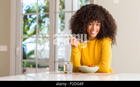 African American donna mangiare insalata di pasta con una faccia felice in piedi e sorridente con un sorriso sicuro che mostra i denti Foto Stock