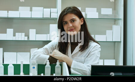Sorridendo felice fiducioso donna giovane farmacista appoggiato su una scrivania in farmacia dando la telecamera una bella grande caldo sorriso amichevole Foto Stock