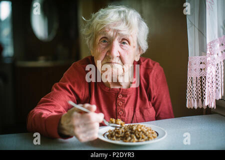 Donna anziana mangia porridge di grano saraceno seduti a tavola. Foto Stock