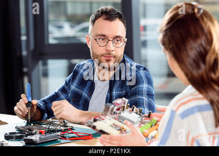 Donna che mantiene il circuito stampato mentre engineer la saldatura di parti di un computer Foto Stock