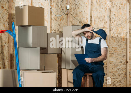 Caricatore stanco uomo checklist di riempimento durante la seduta di scatole Foto Stock