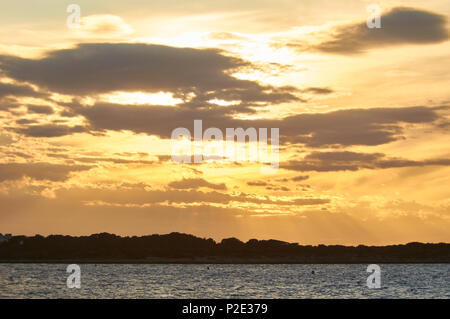 Tramonto Dorato a Caló de s'Oli con raggi di sole e nuvole retroilluminato da Sa Boca nel Parco Naturale di Ses Salines (Formentera, isole Baleari, Spagna) Foto Stock