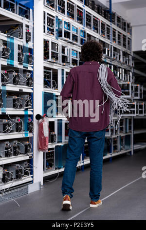 Vista posteriore del computer engineer con cavi ethernet sulla spalla a cryptocurrency fattoria di data mining Foto Stock