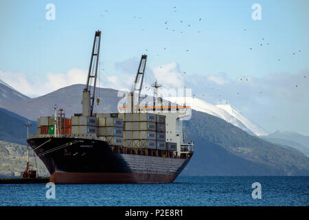 Un contenitore grande nave giace nel piccolo porto di Ushuaia, nel sud dell'Argentina. Arti marziali le montagne sono in background. Foto Stock