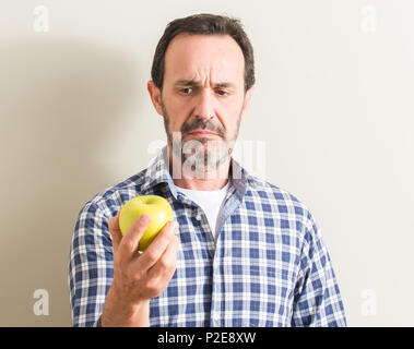 Senior man tenendo una mela verde con un fiducioso espressione sul viso intelligente pensare grave Foto Stock