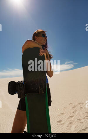 Donna con sandboard in piedi nel deserto Foto Stock