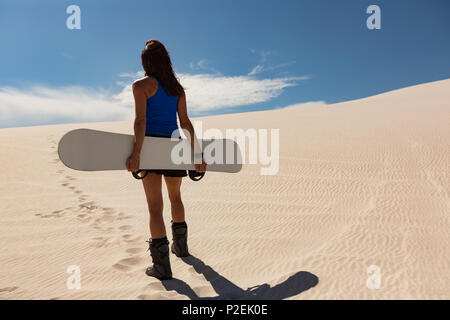 Donna con sandboard in piedi nel deserto Foto Stock