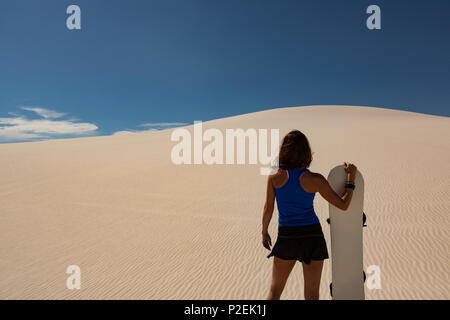 Donna con sandboard in piedi nel deserto Foto Stock