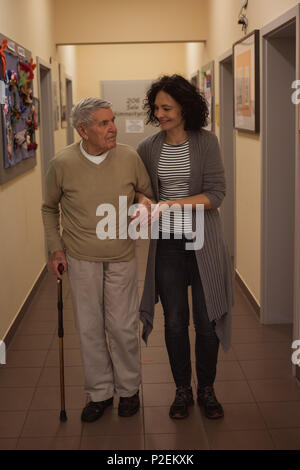 Custode assiste senior uomo mentre passeggiate in corridoio Foto Stock