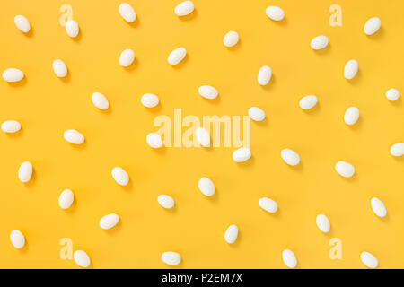 Il cioccolato bianco caramelle sparse su gioiosa di colore giallo brillante background. Foto Stock