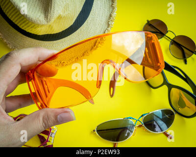 Piatto viaggiatore laici accessori. Raccolta a mano la Orange Estate bicchieri di plastica e tanti tipi di occhiali da sole e spiaggia Hat sul giallo limone sfondo. Top V Foto Stock