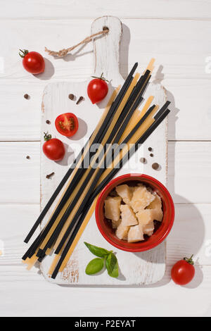 Vista dall'alto di vari prodotti alimentari italiani con il bianco e nero di spaghetti bianco sul tagliere di legno Foto Stock