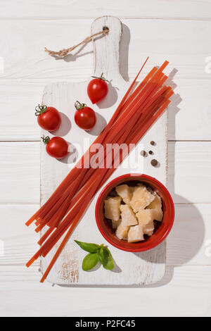 Vista dall'alto di vari prodotti alimentari italiani con spaghetti di rosso su bianco tagliere di legno Foto Stock