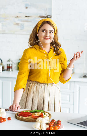 Bella donna ascoltando musica con lo smartphone in cucina Foto Stock