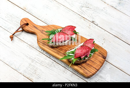 Gustosi antipasti e tagliata a fettine sottili di salame piccante su pane con formaggio ed erbe su un tagliere con spazio di copia Foto Stock