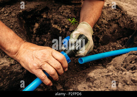 Lavoratore si collega un tubo flessibile dell'acqua prevista nel terreno per innaffiare il giardino Foto Stock