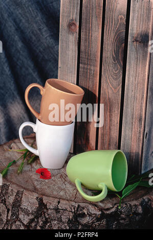 Nuovo tazze su un ceppo di legno con un fiore rosso, su uno sfondo di tessuto grigio e una scatola di legno. Ancora in vita. Foto di piatti Foto Stock