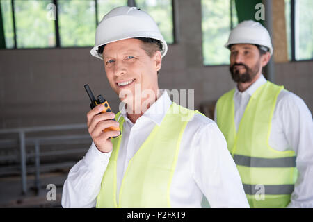 Matura sorridente costruttore di attrezzature professionali parlando al radio set Foto Stock