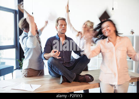 Imprenditore rilassato meditando nella posizione del loto mentre i colleghi che celebra il successo Foto Stock